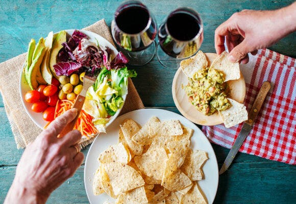 Table with guacamole avocado and wine, while two people eat.