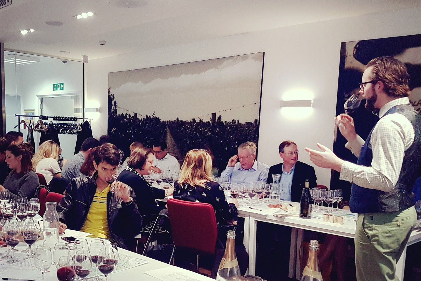 Man smelling wine to two tables of adults with multiple wine glasses each
